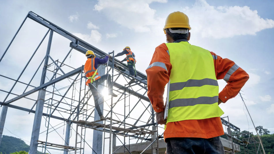 A construction worker is looking at two workers on a frame building.